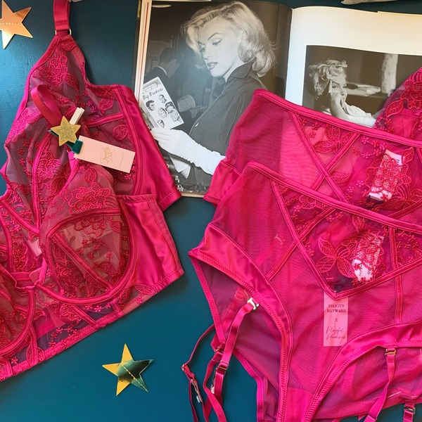 Pink embroidered longline bra and suspender briefs on table beside Marilyn Monroe book and gold stars